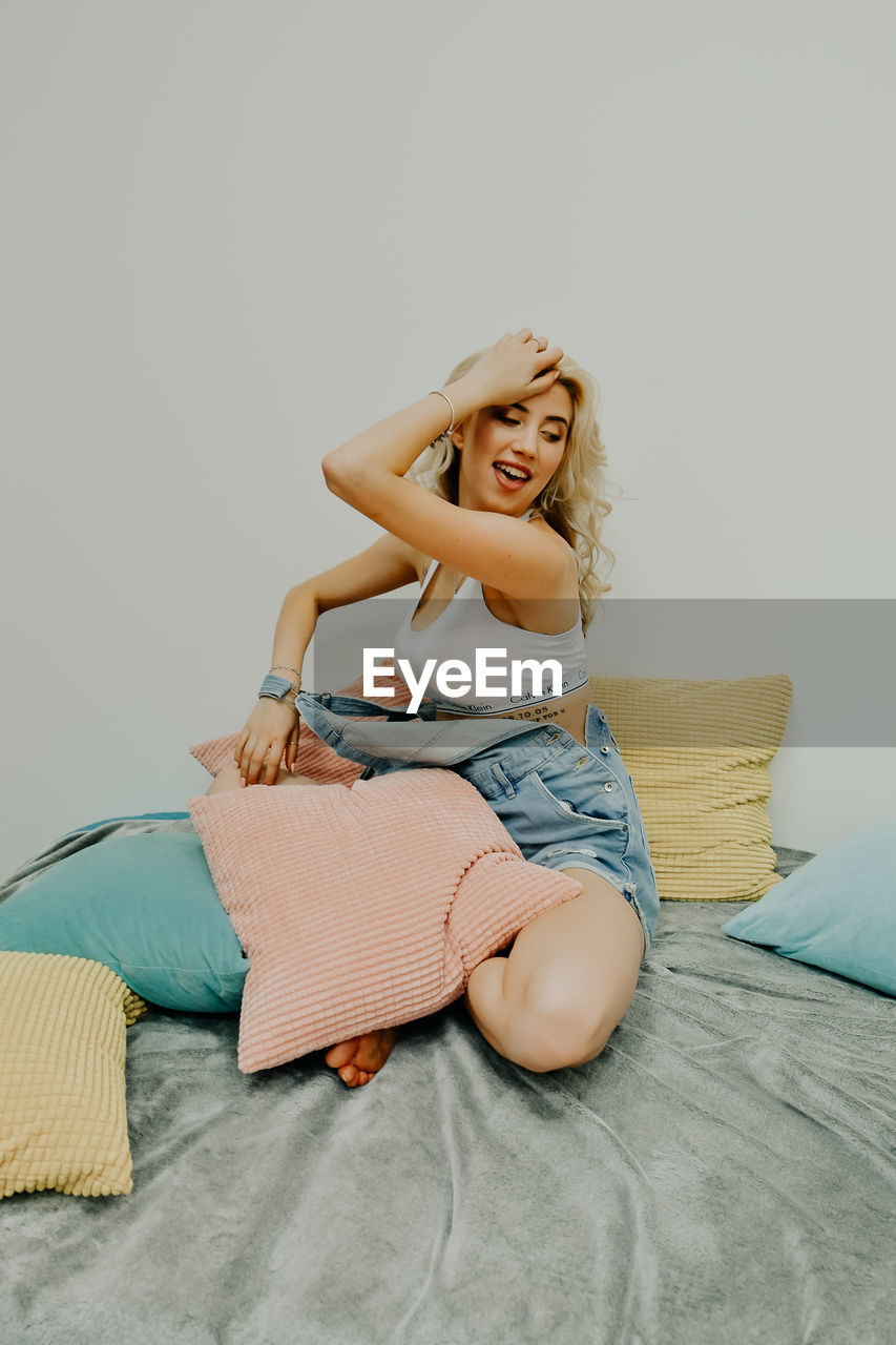 Happy young woman sitting on bed at home