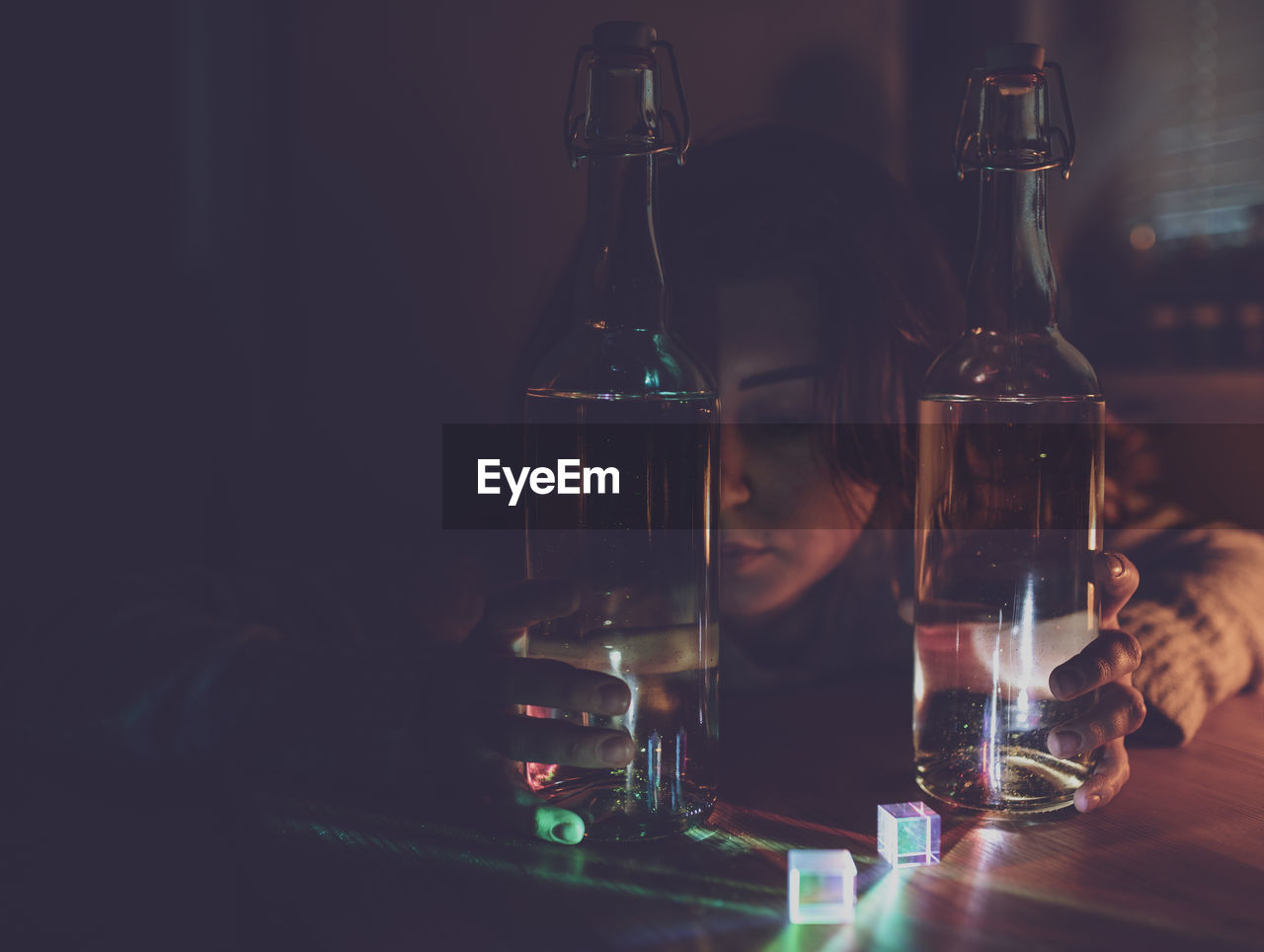 Thoughtful woman with wine bottles on table in darkroom