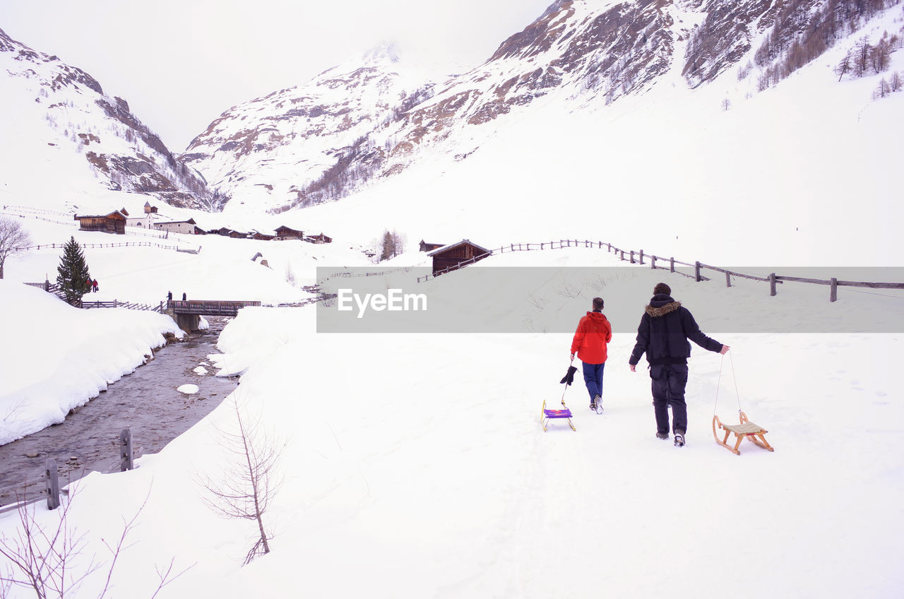 REAR VIEW OF MEN SKIING ON SNOWCAPPED MOUNTAIN