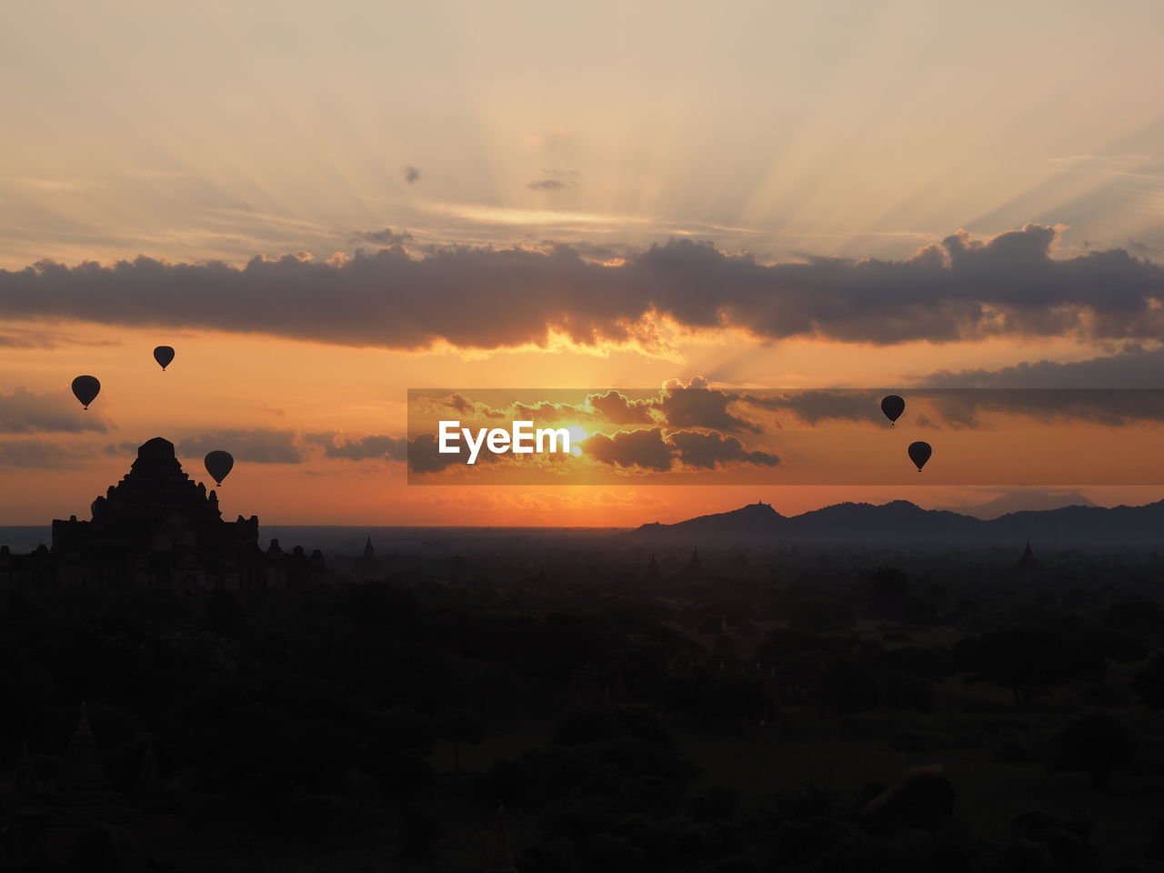 Silhouette hot air balloons flying over ancient temples against sky during sunset