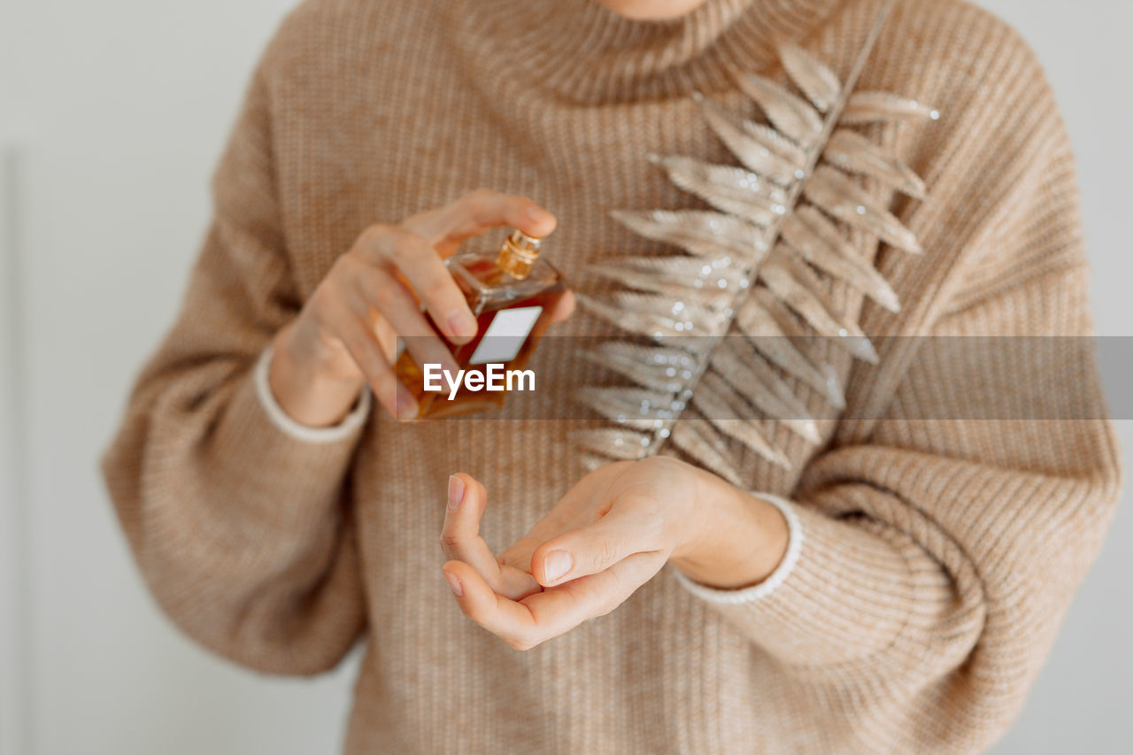 Midsection of woman spraying perfume on hand