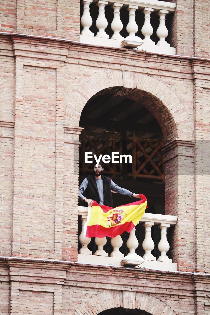 PORTRAIT OF SENIOR MAN STANDING AGAINST BUILDING