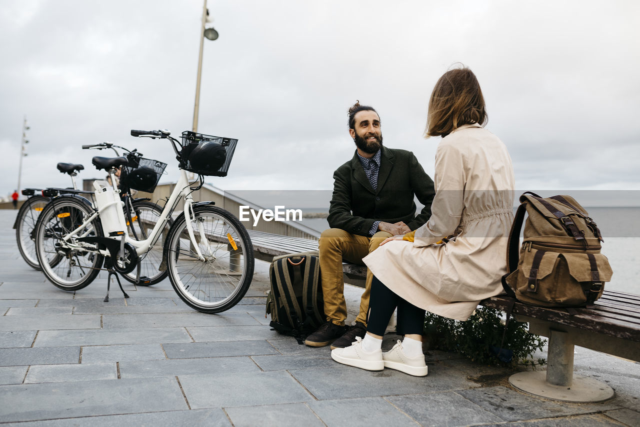 Couple sitting on a bench at beach promenade next to e-bikes talking