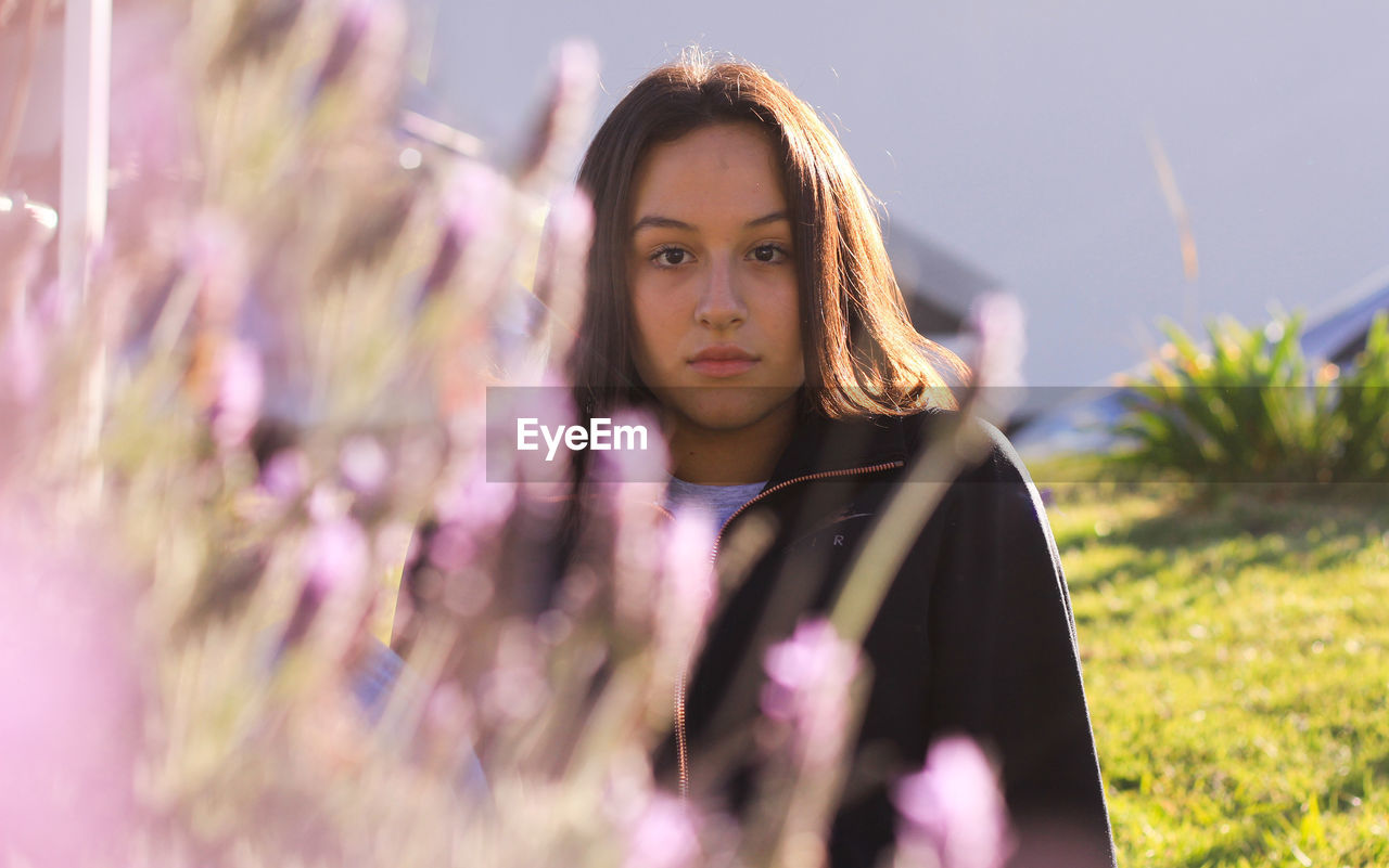 PORTRAIT OF YOUNG WOMAN AGAINST PINK PLANTS