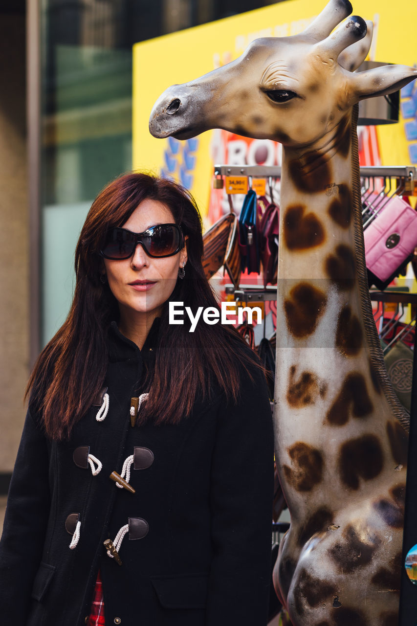 Woman wearing sunglasses while standing by giraffe sculpture