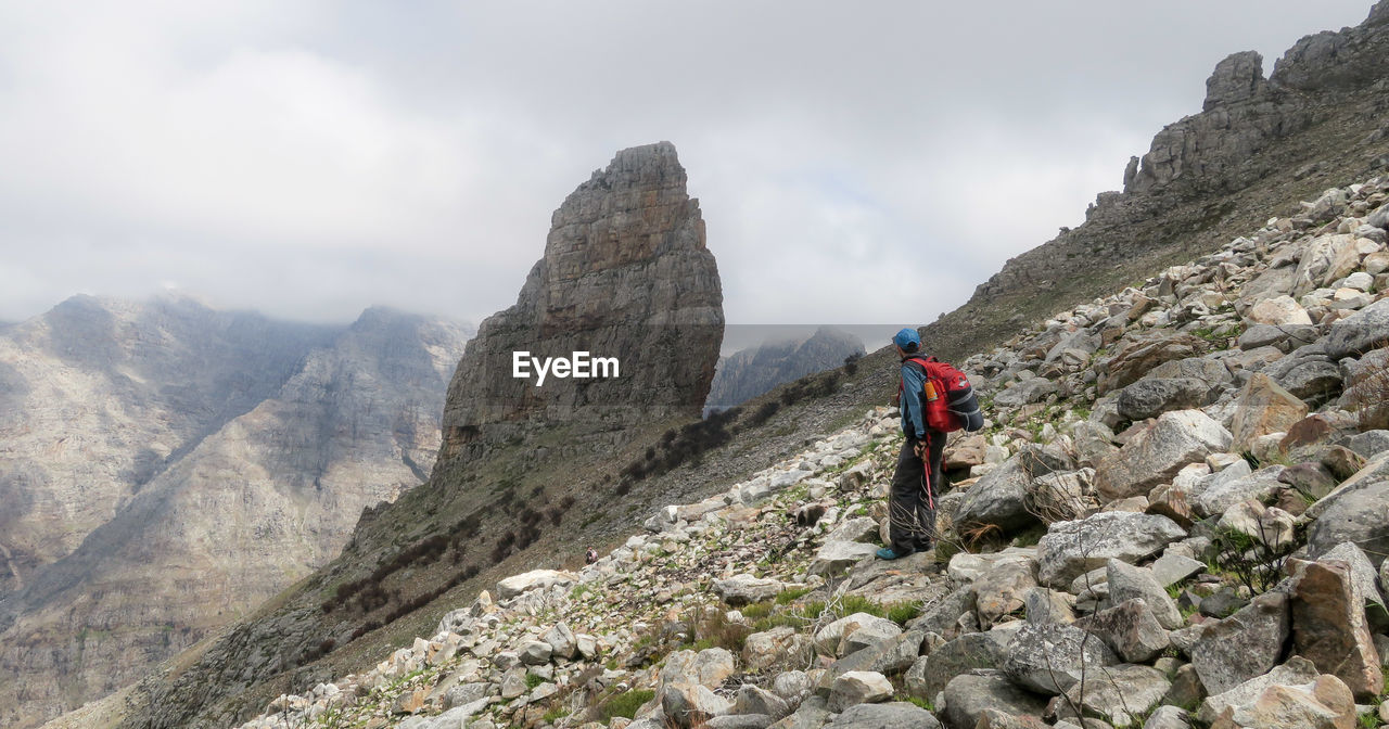 REAR VIEW OF MAN STANDING ON ROCKY MOUNTAIN