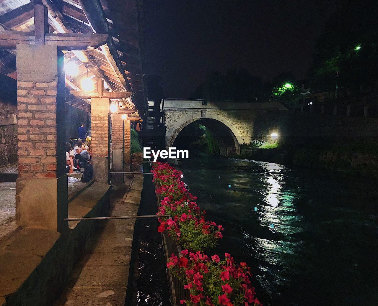 BRIDGE OVER RIVER AGAINST ILLUMINATED STREET LIGHT AT NIGHT