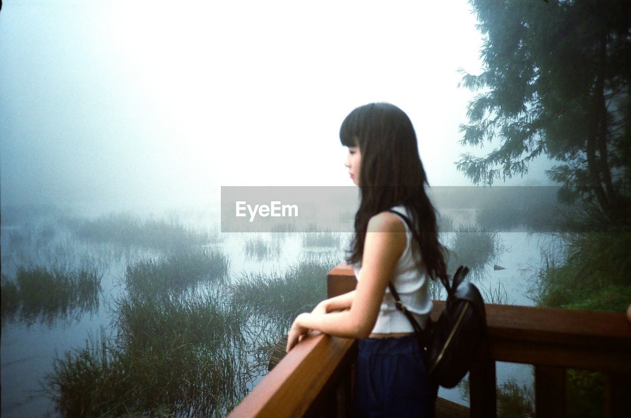 Side view of woman looking at lake during foggy weather