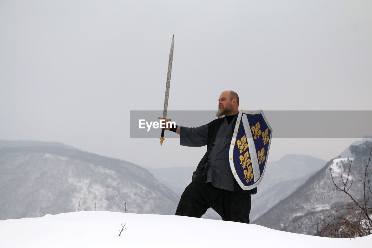 MAN STANDING ON SNOW COVERED MOUNTAIN AGAINST SKY