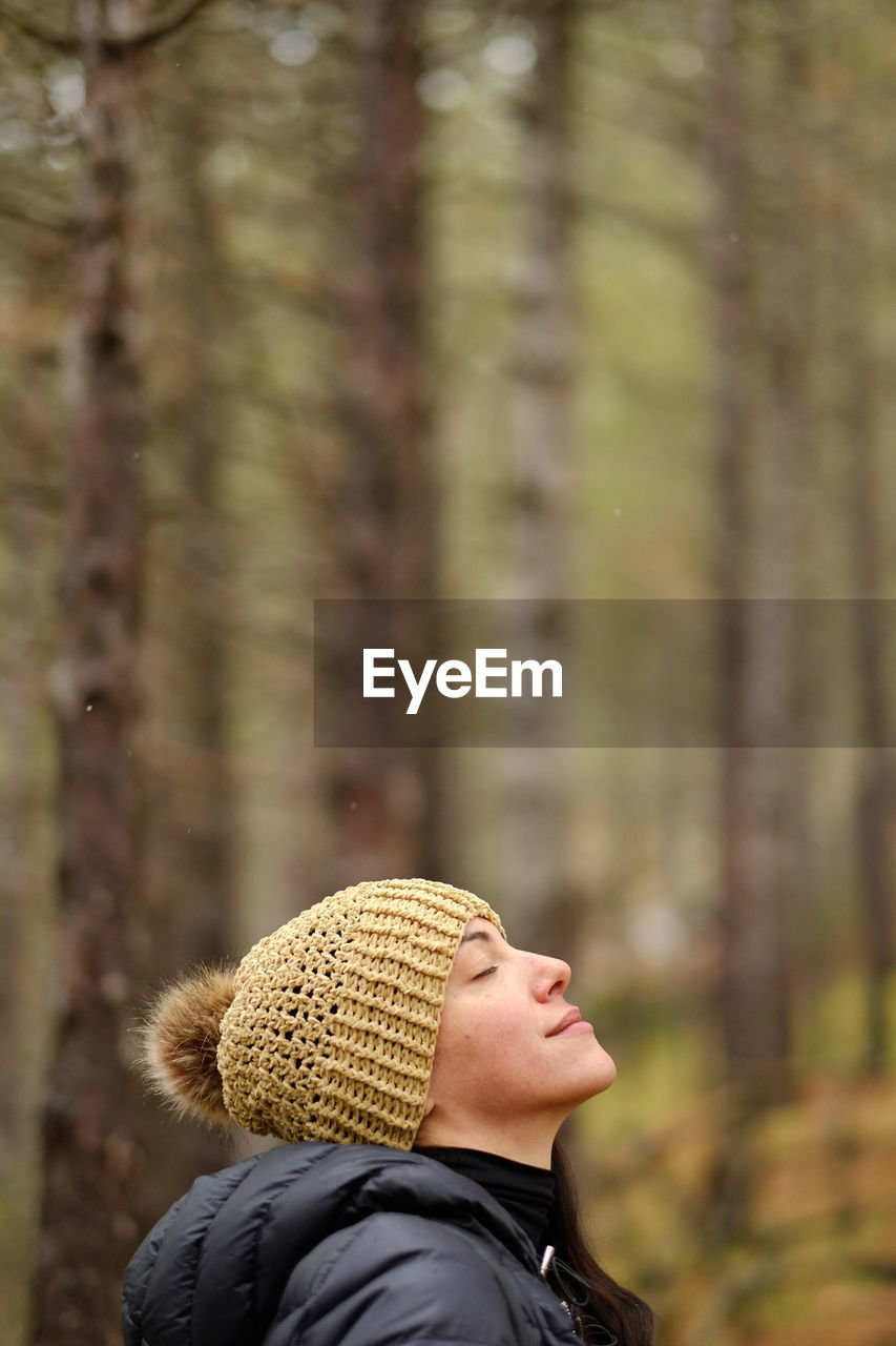 Portrait of young woman looking away with hat in woods