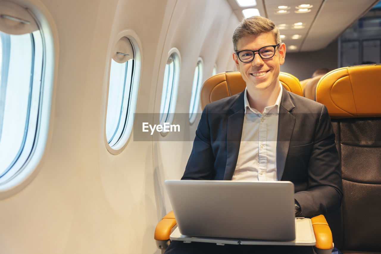 During a flight, a businessman in formal attire and glasses looks out the plane window 