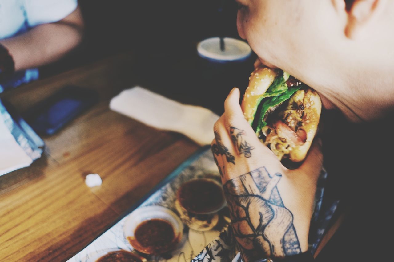 Midsection of man eating burger in restaurant