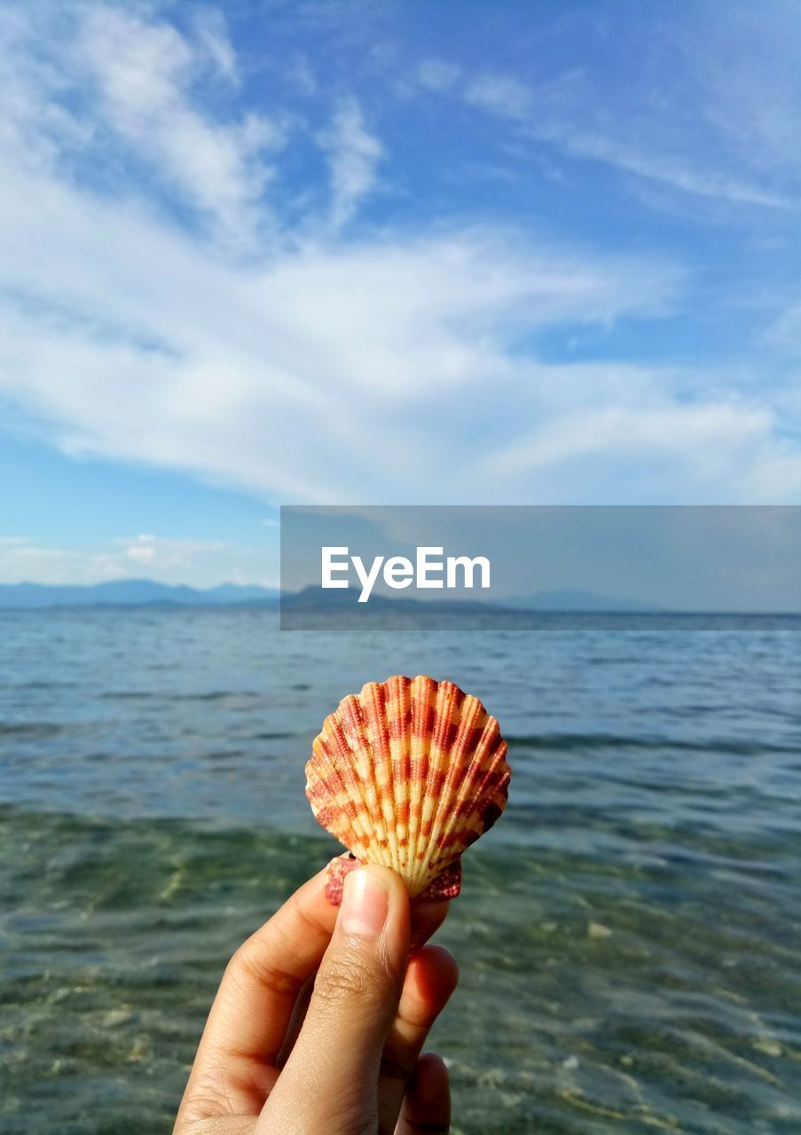 CLOSE-UP OF PERSON HOLDING ICE CREAM AGAINST SEA