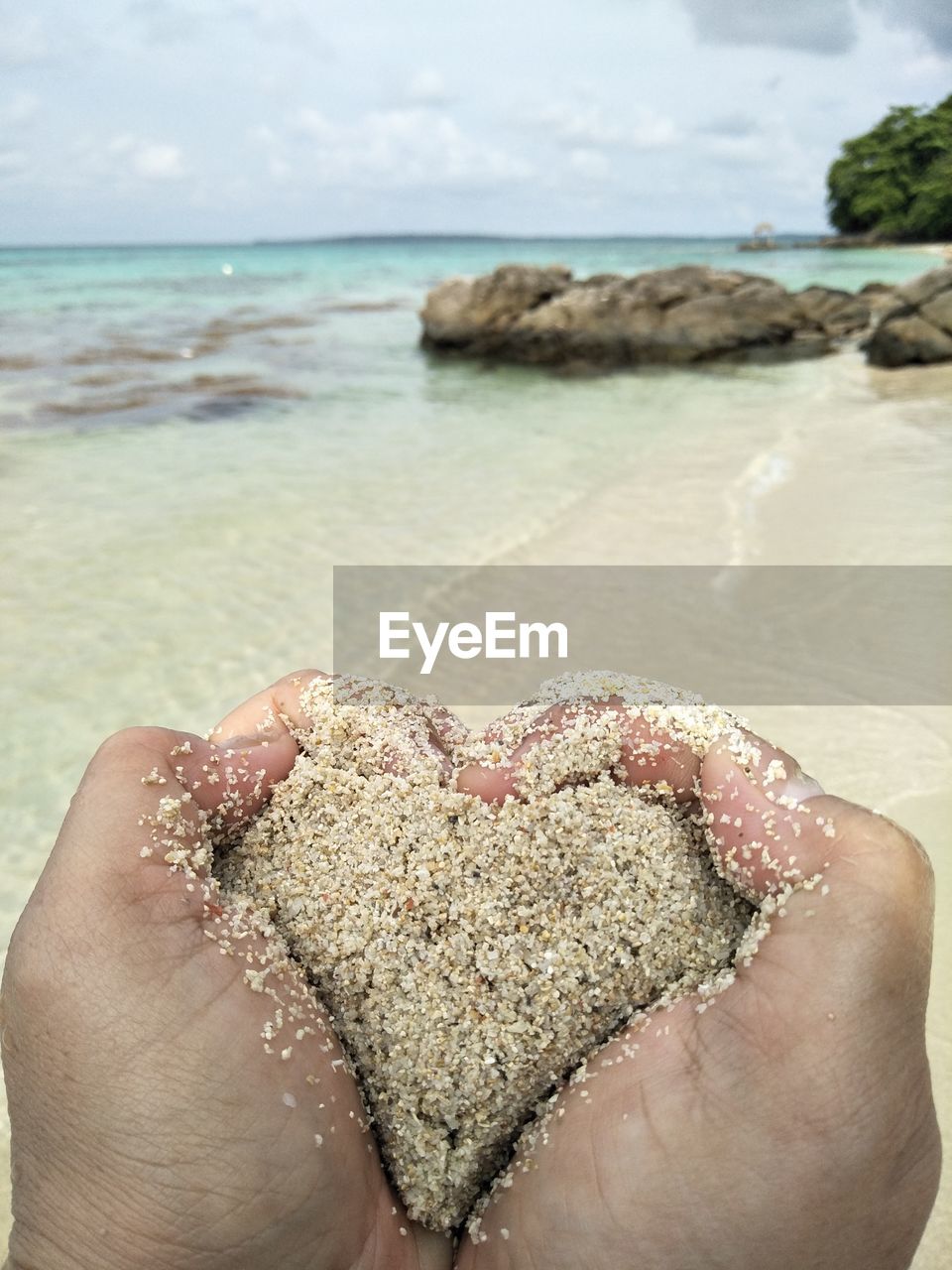 Cropped hands forming heart shape with wet sand at beach