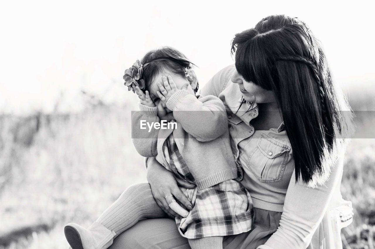 REAR VIEW OF MOTHER AND DAUGHTER SITTING ON FLOOR