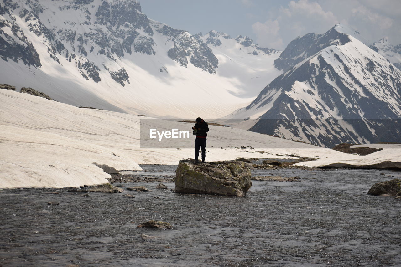 Man standing on rock against snowcapped mountains