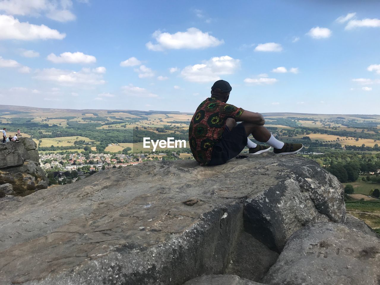 Side view of man sitting on cliff against sky