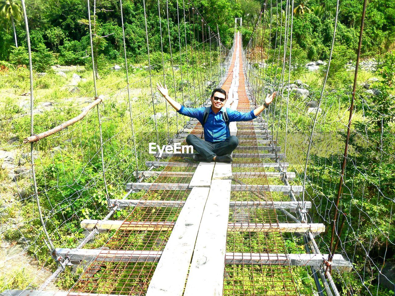 Full length of man sitting on footbridge in forest