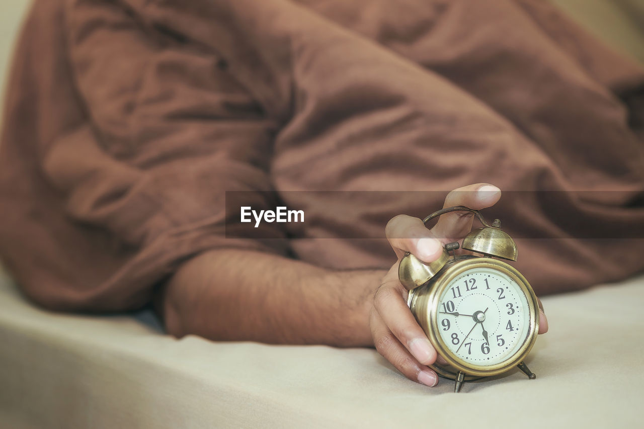 Close-up of hand holding alarm clock on bed