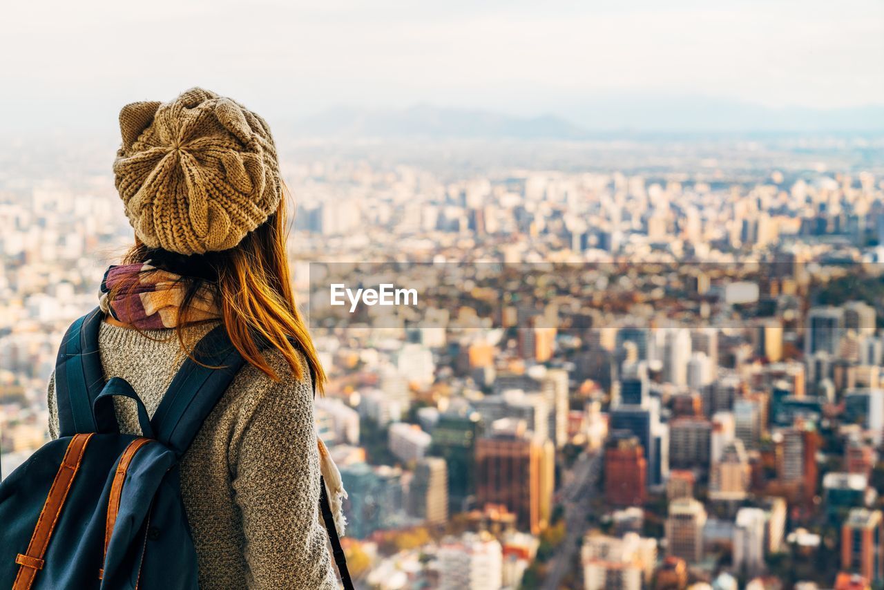 Rear view of young woman with backpack standing against cityscape