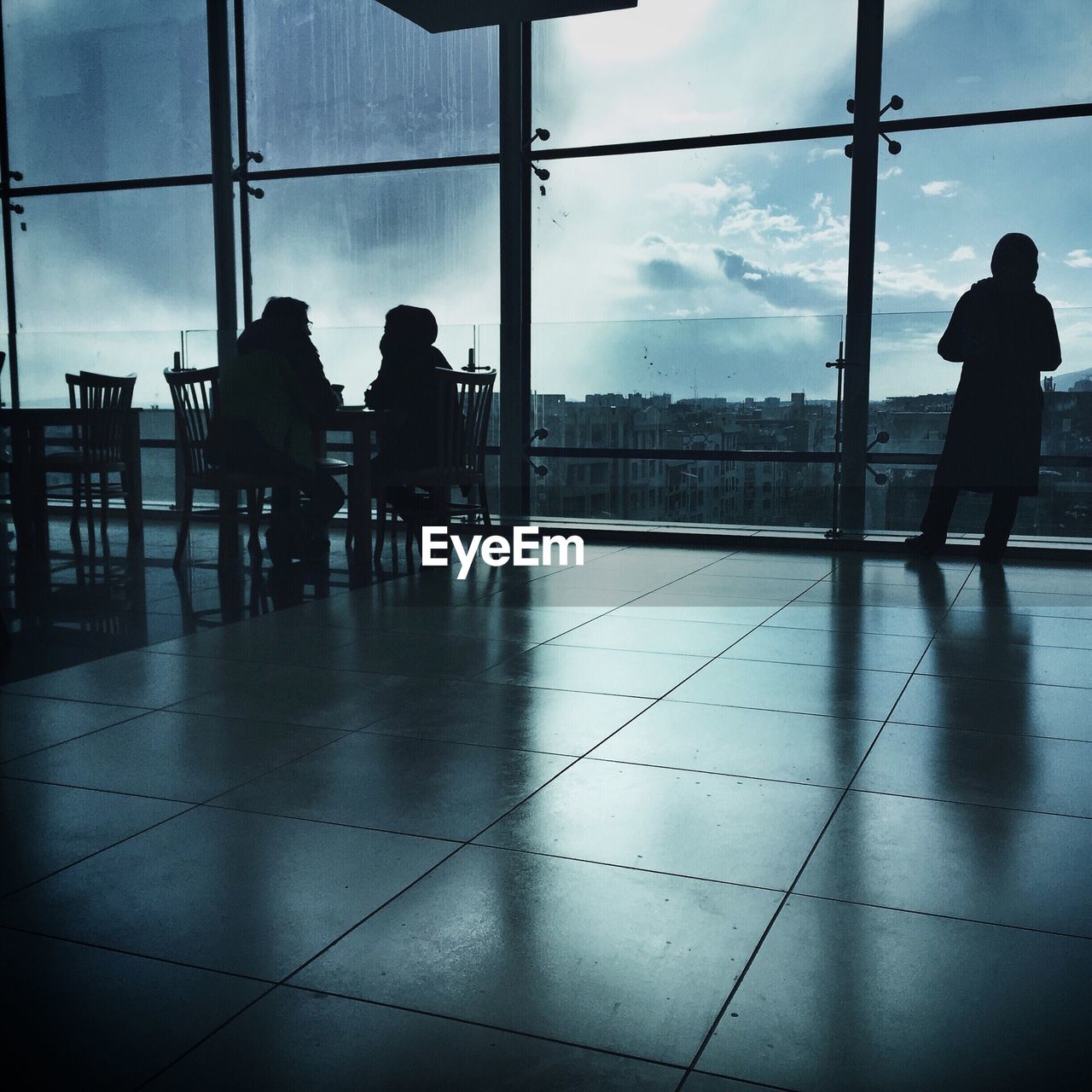 Silhouette people at cafe by window against sky