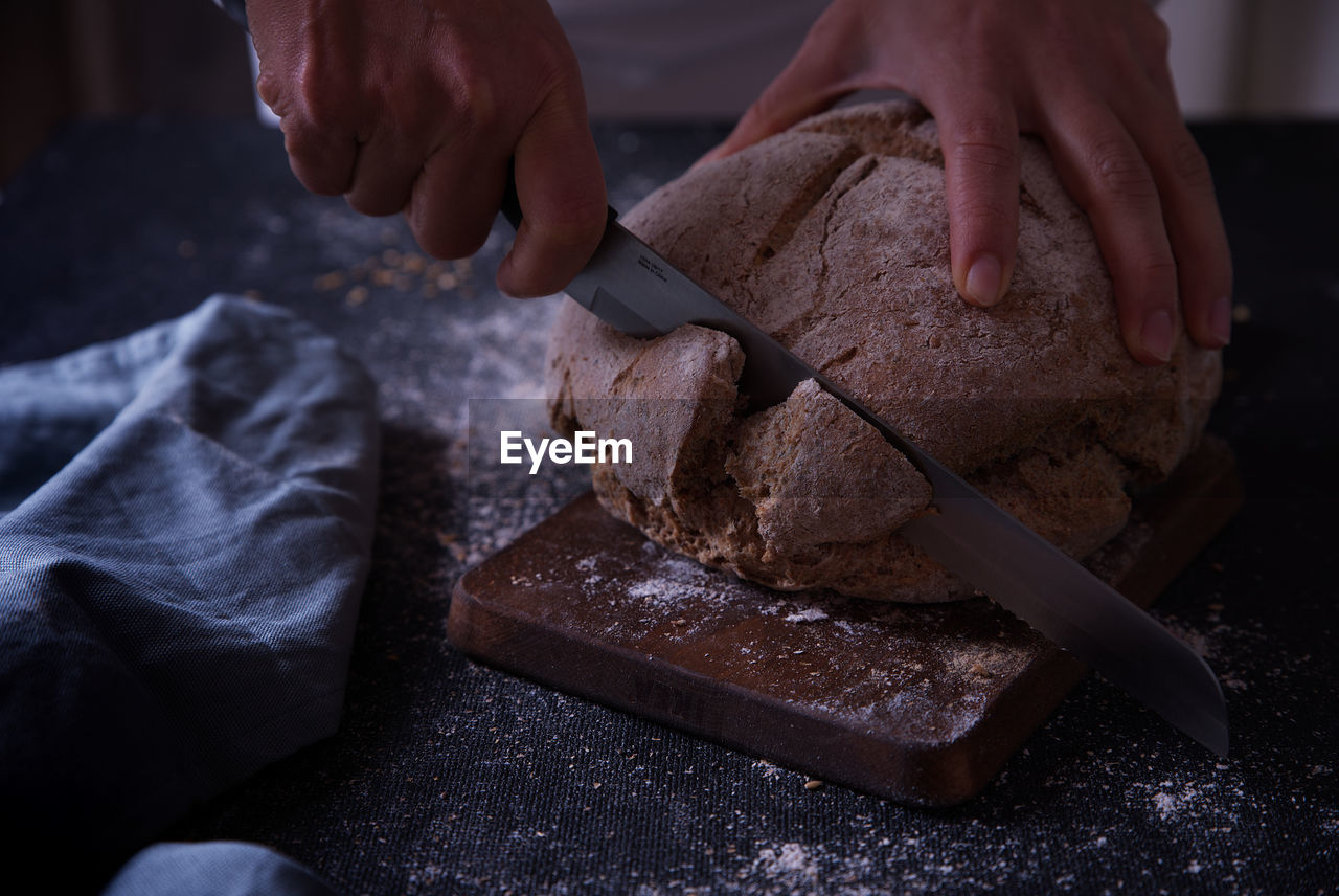 Hands slicing fresh bread, on dark background.