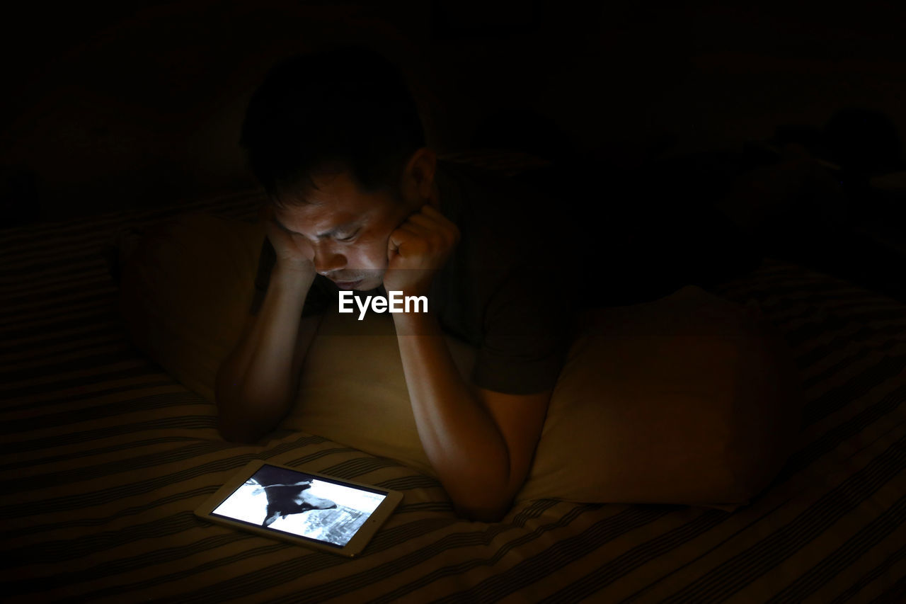 High angle view of young man using digital tablet on bed in darkroom