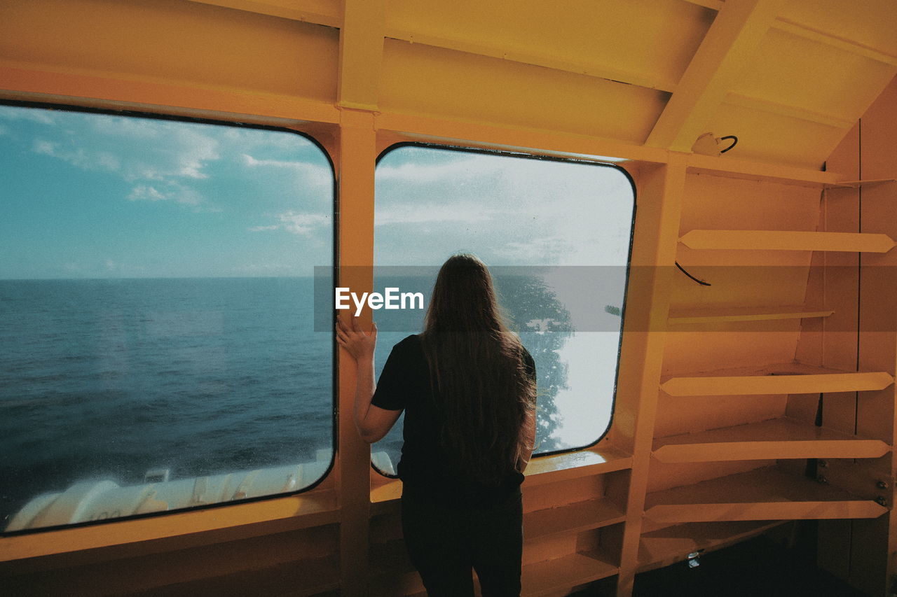 Rear view of woman looking through boat window
