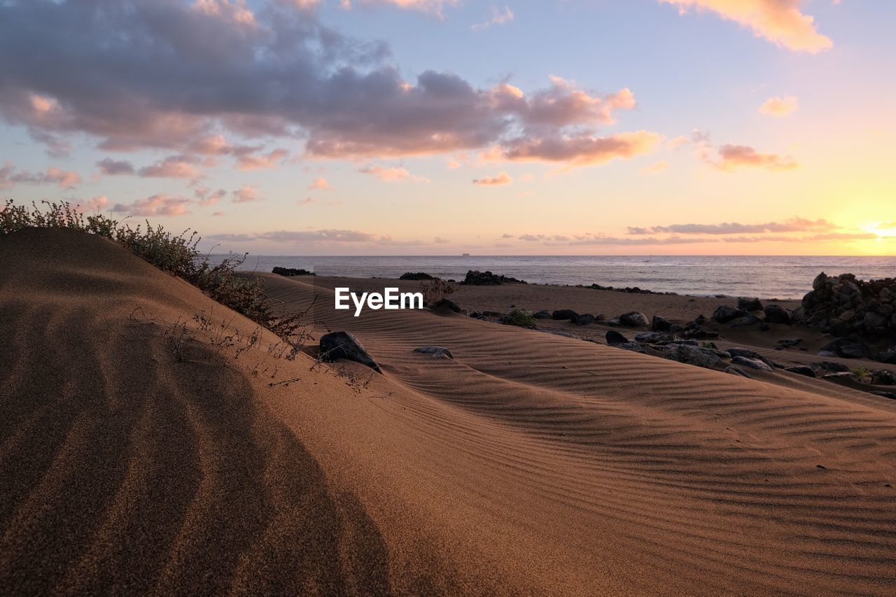 rear view of man walking on beach against sky during sunset