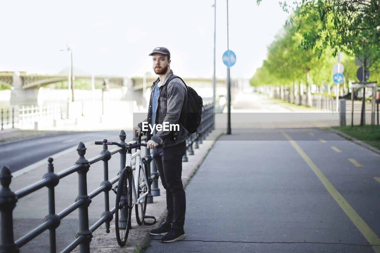 Man with bicycle standing on road in city