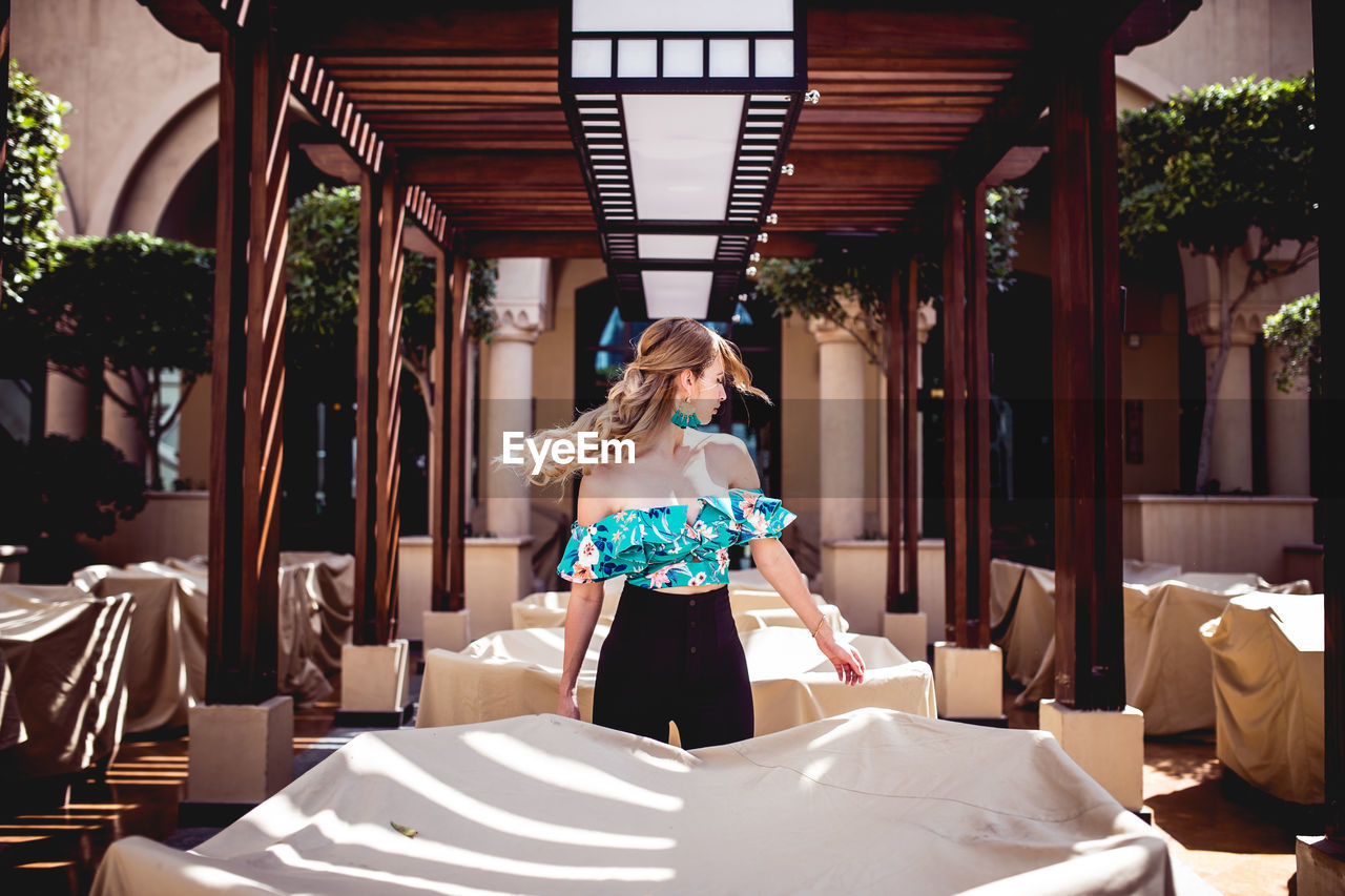 Fashionable woman standing amidst covered furniture at restaurant