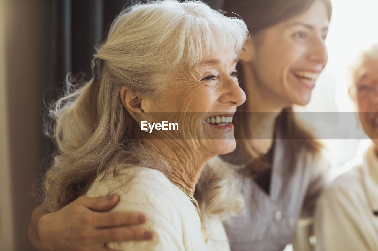 Happy elderly woman by female caregiver at nursing home