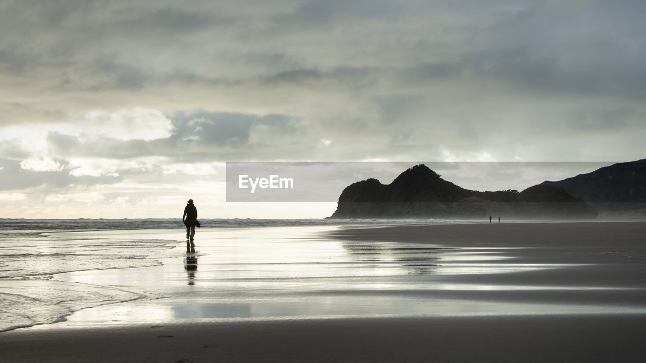Silhouette man walking on beach against sky