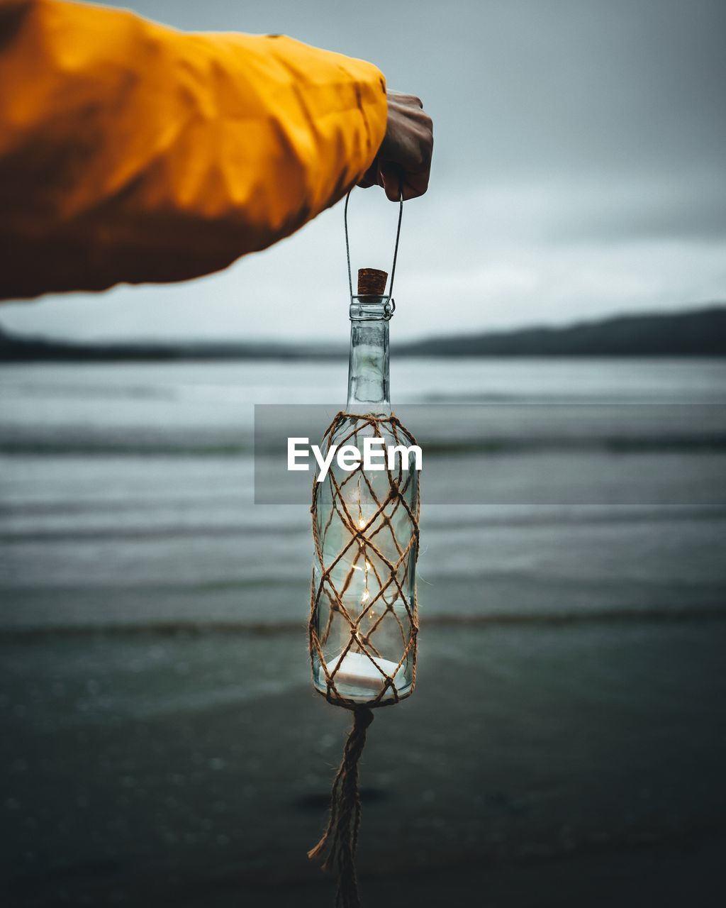 Close-up of hand holding illuminated bottle at beach