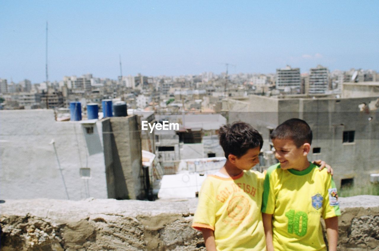 REAR VIEW OF BOYS AND CITYSCAPE AGAINST SKY