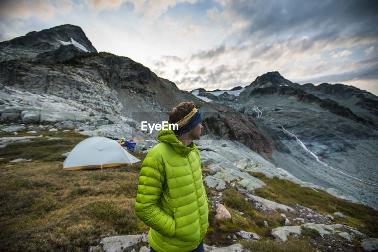 Hiker standing next to tent looking at mountain view.