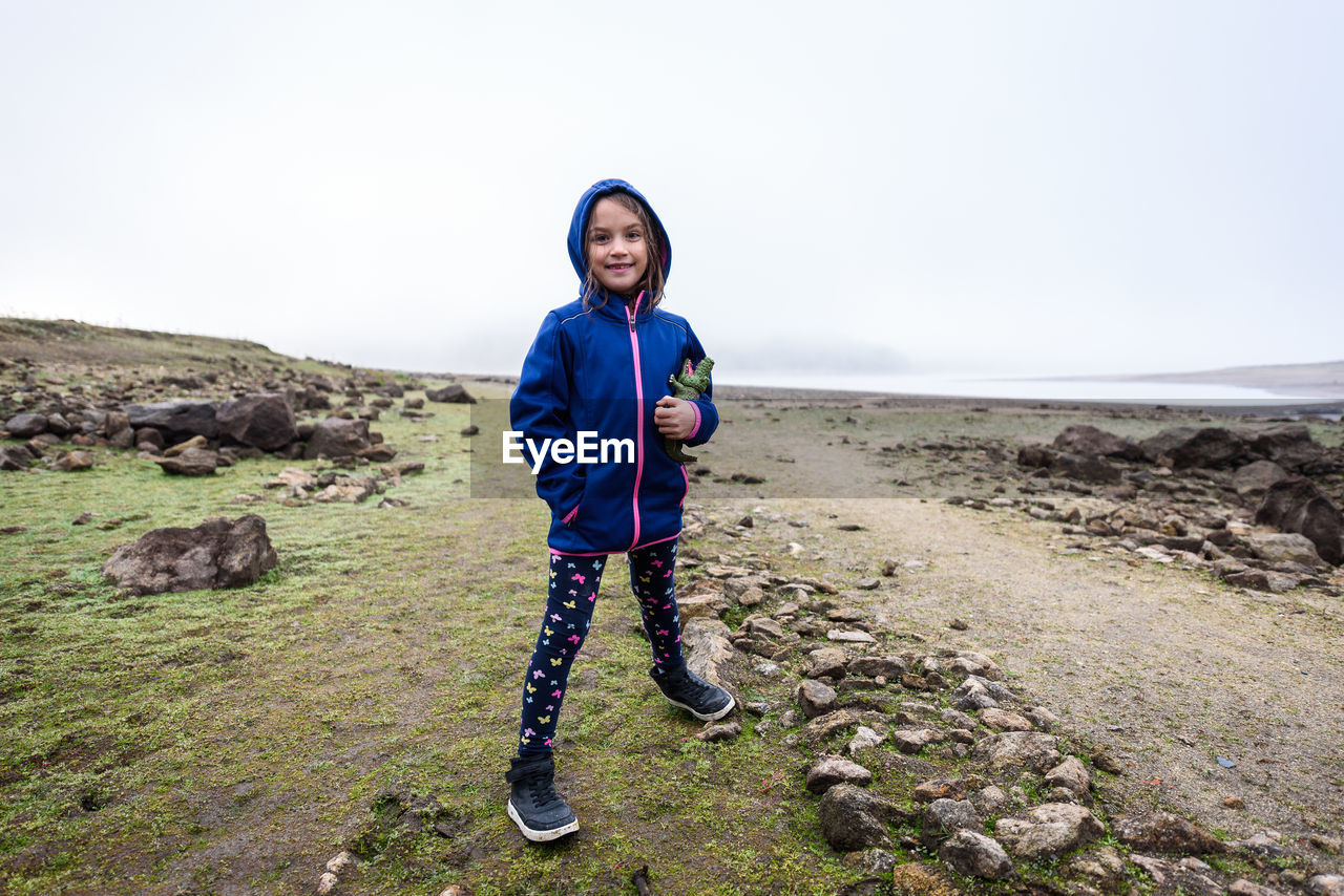 Portrait of smiling girl standing on field against sky