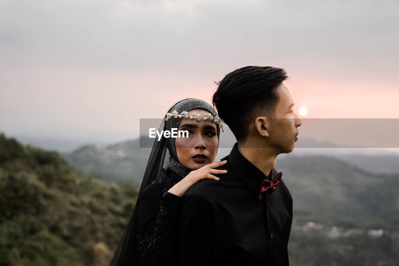 YOUNG COUPLE LOOKING AWAY AGAINST MOUNTAIN