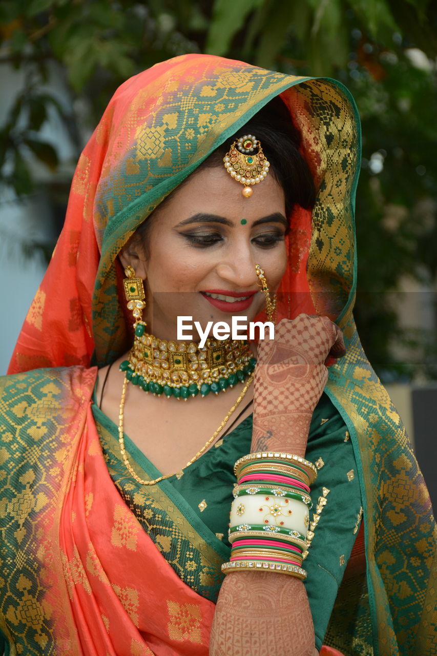 Smiling young bride in sari looking away against trees