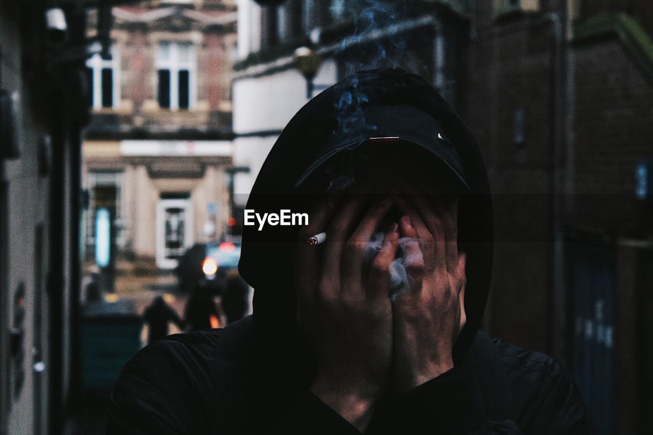 Close-up of man smoking cigarette while covering face with hands