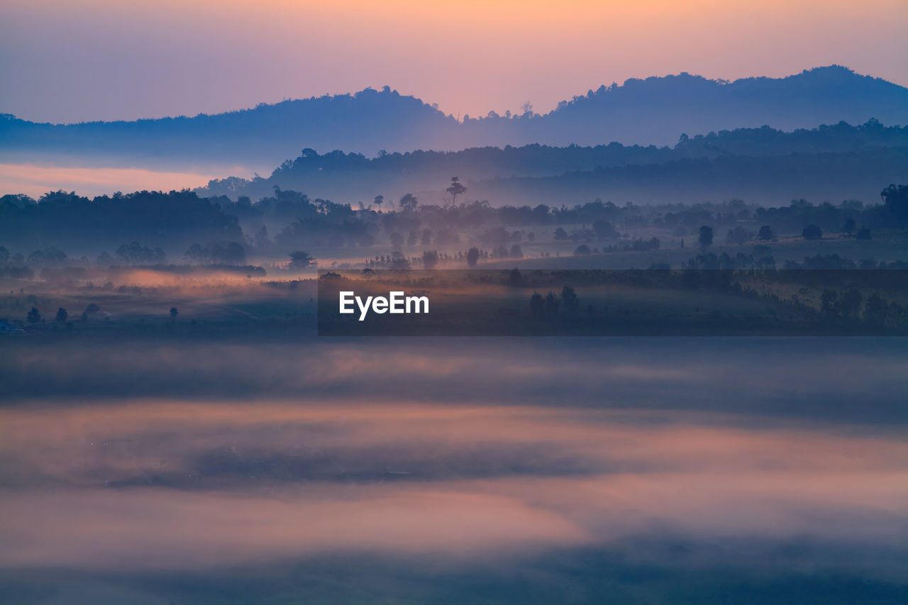 Scenic view of silhouette landscape during foggy weather at sunset