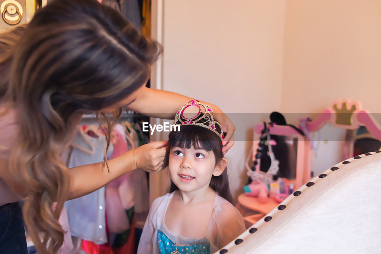 Mom placing a crown on daughters head, girl looking up at mom.