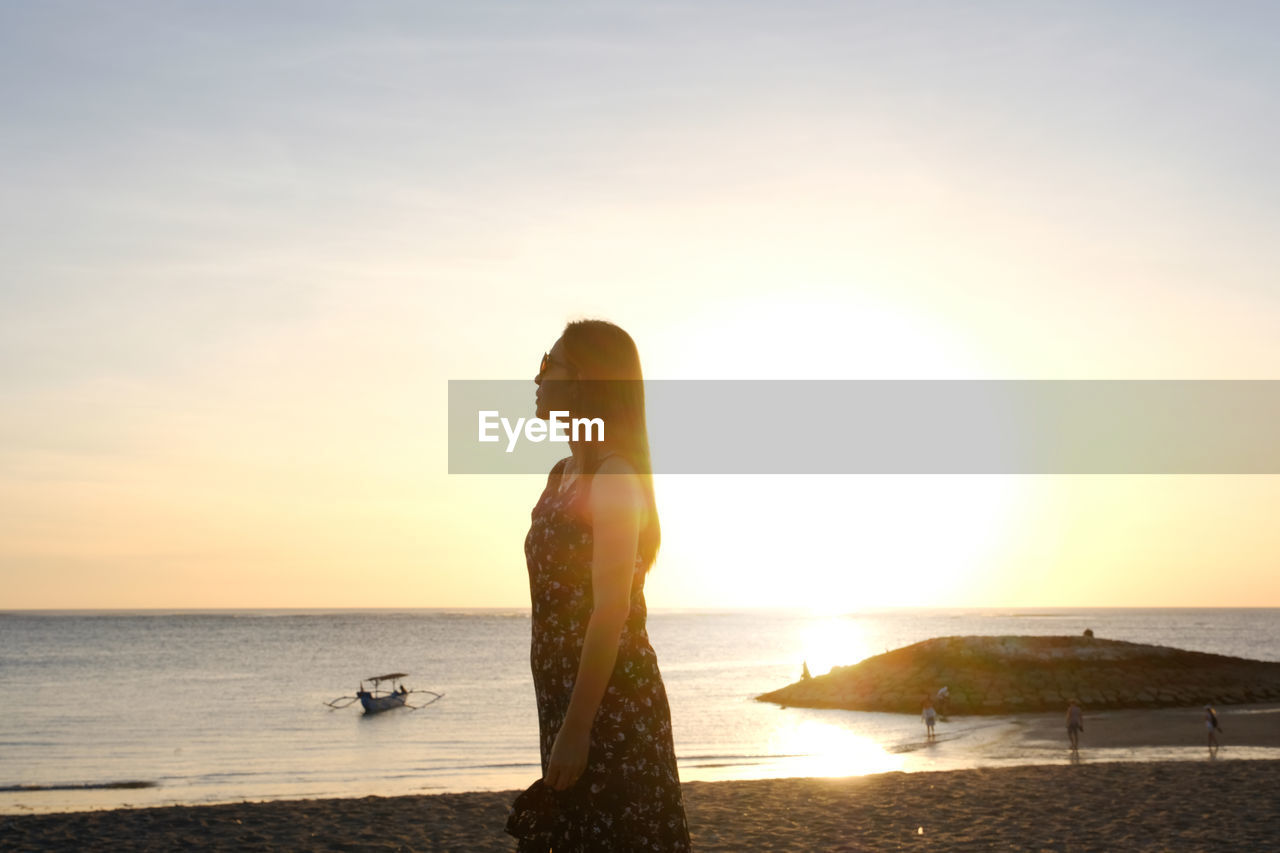 Woman looking at sea against sky during sunset