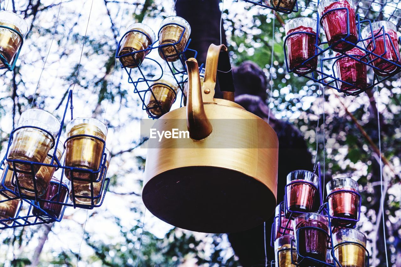 Low angle view of artwork made from teapot and glasses hanging to tree