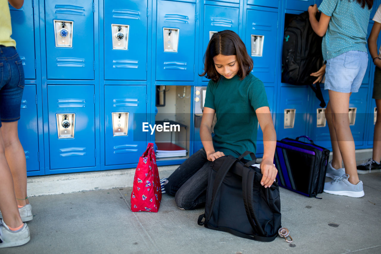 Tween girl looks into her backpack as she organizes her locker