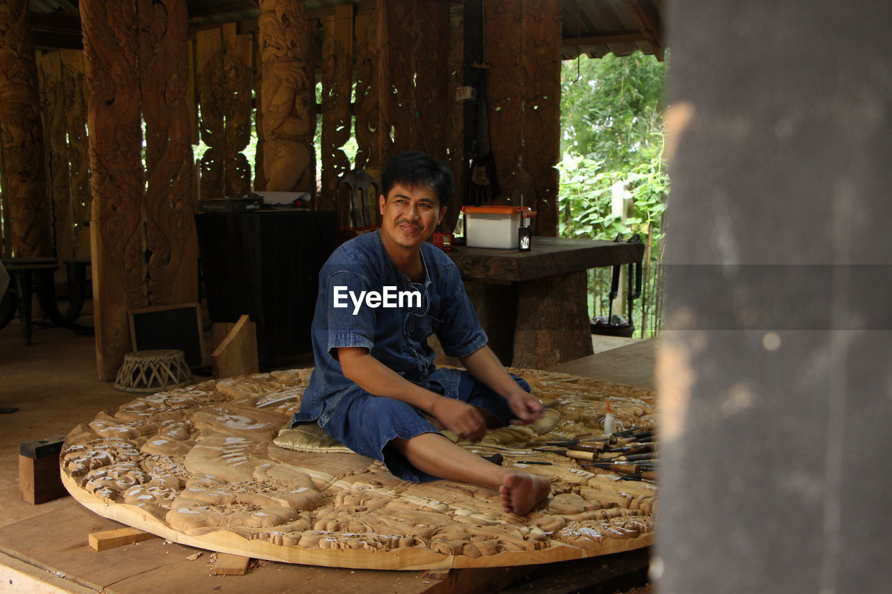 Man carving wood while sitting at workshop