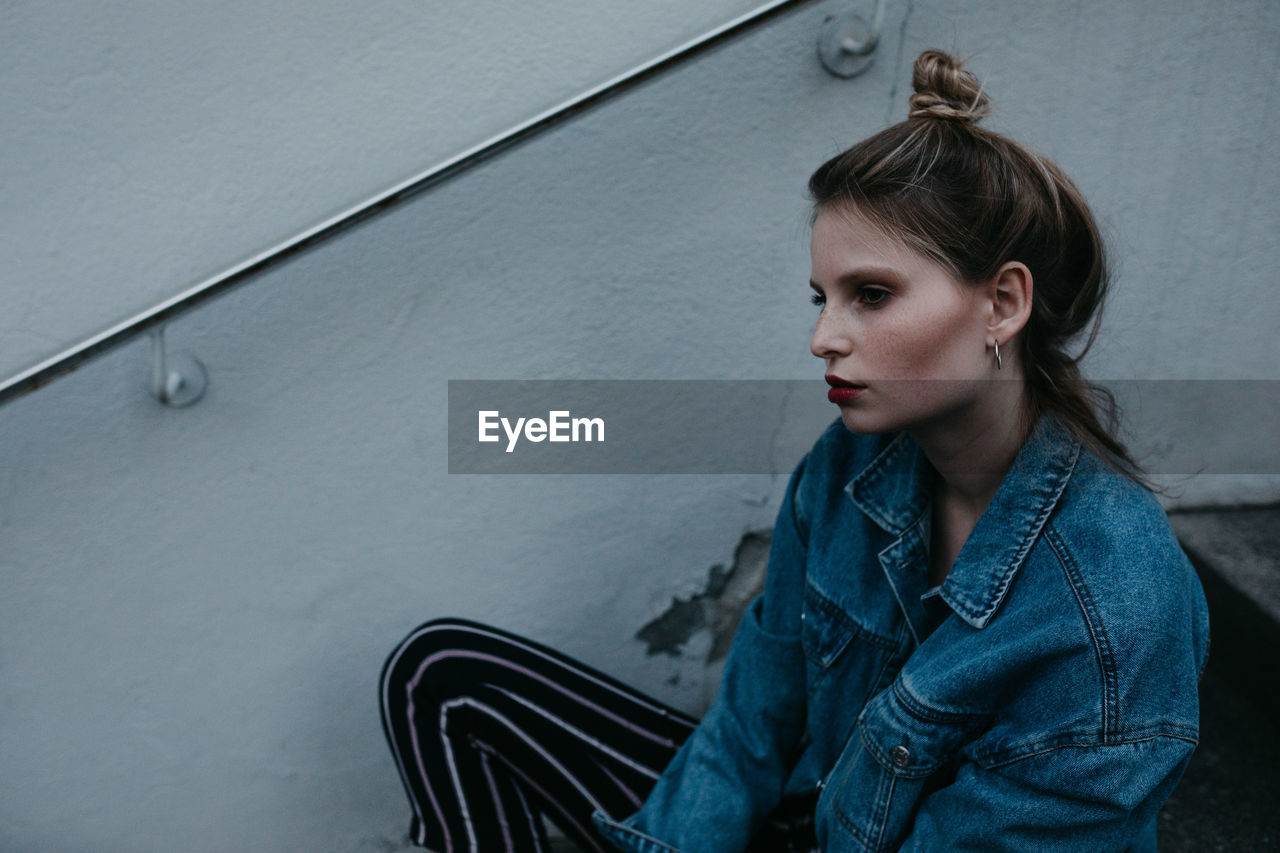 Thoughtful woman wearing denim jacket while sitting outdoors