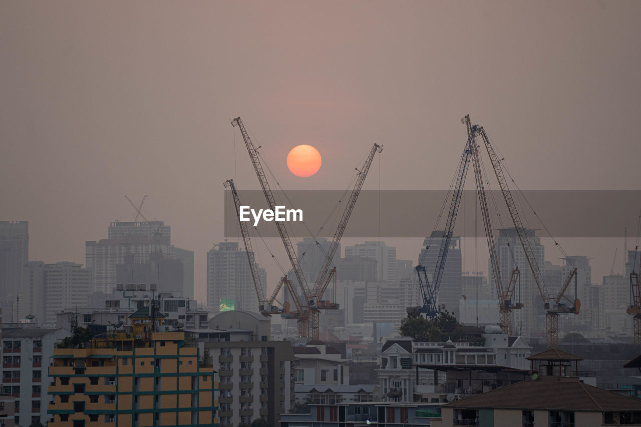 Cranes in city against sky during sunset