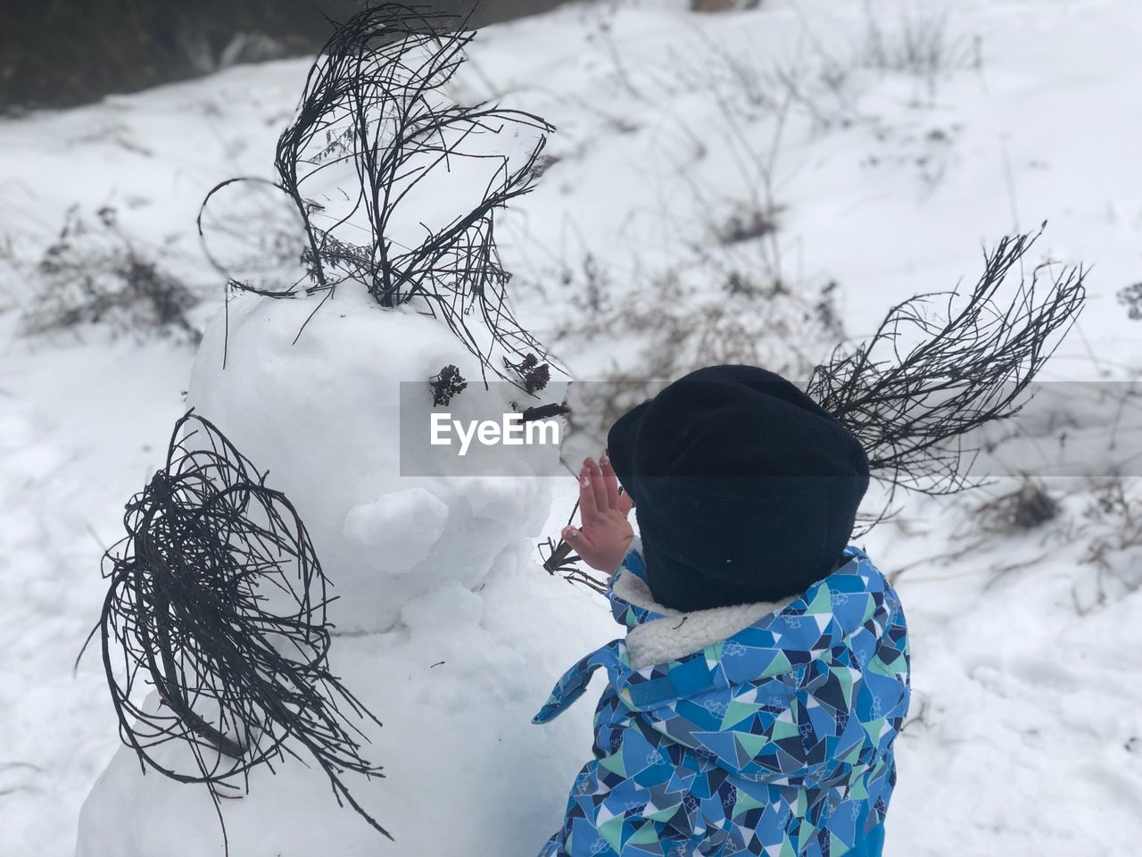 Full length of boy looking at snowman in winter
