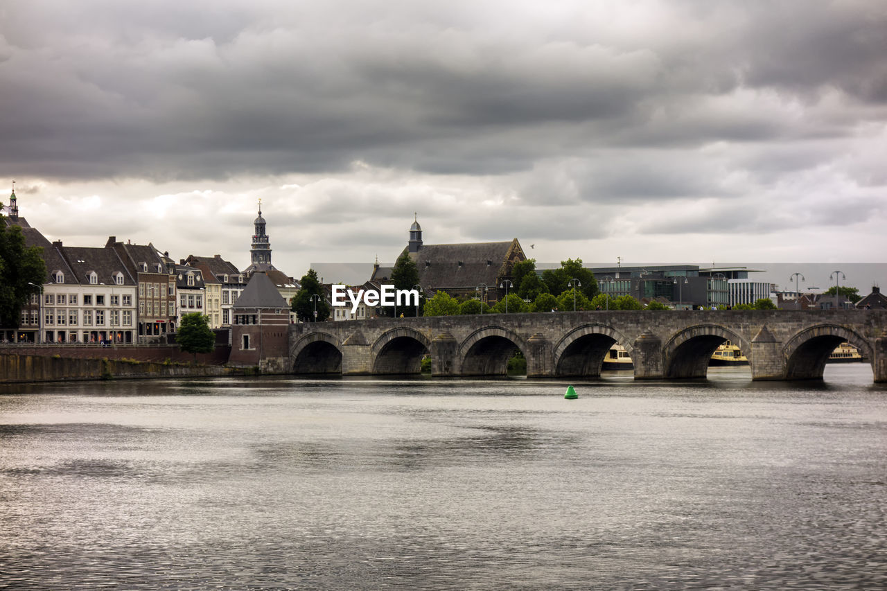 Arch bridge over river by buildings against sky